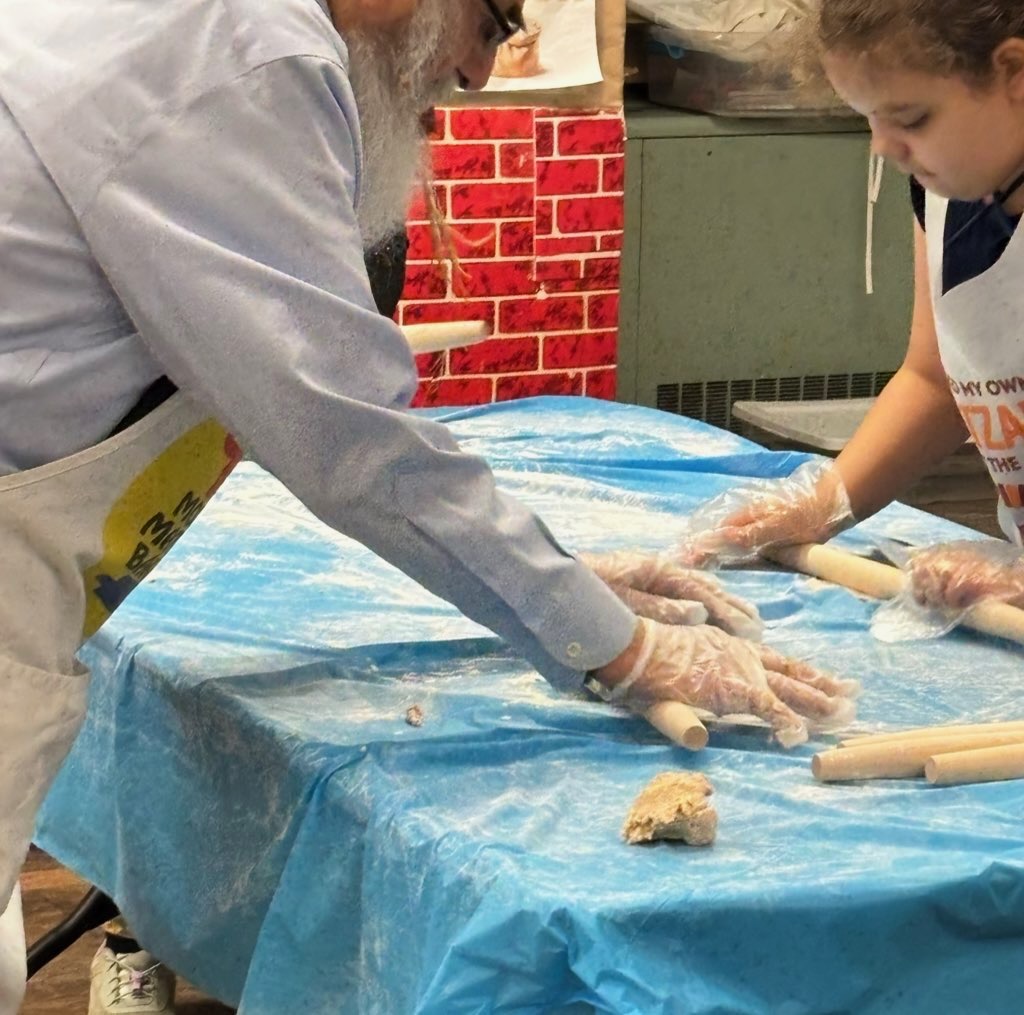 Rabbi Yaakov Rappaport shows children how to prepare and bake matzah.