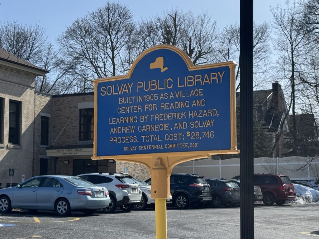 Sign outside Solvay Public Library establishing its existence Sign reads "SOLVAY PUBLIC LIBRARY. Built as a Village center for reading and learning by Frederick Hazard, Andrew Carnegie, and Solvay Process. Total Cost: $28,748"