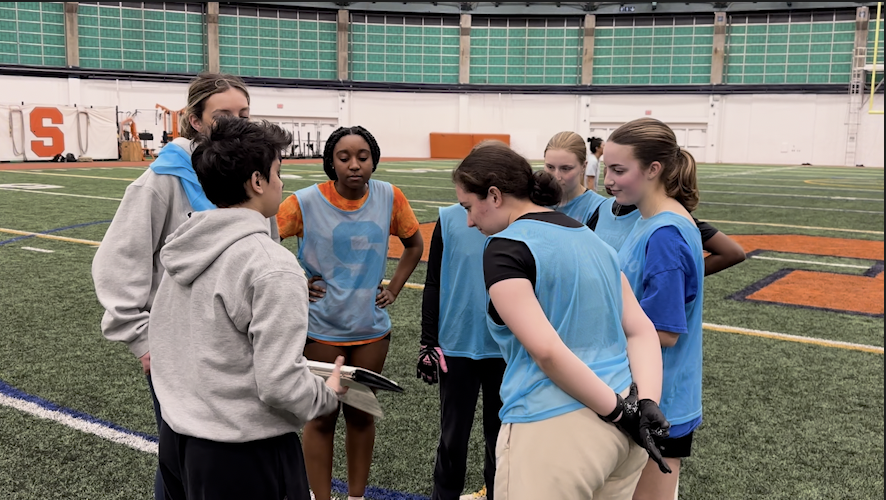 Syracuse women's flag football players huddle around their coach to look at a play