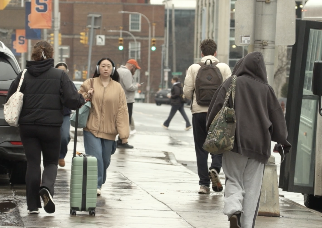 Students walking down the Syracuse University campus with luggage.