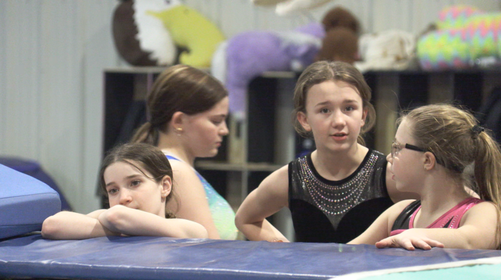 Isabella McMillan stands with teammates during practice inside a trampoline gym.
