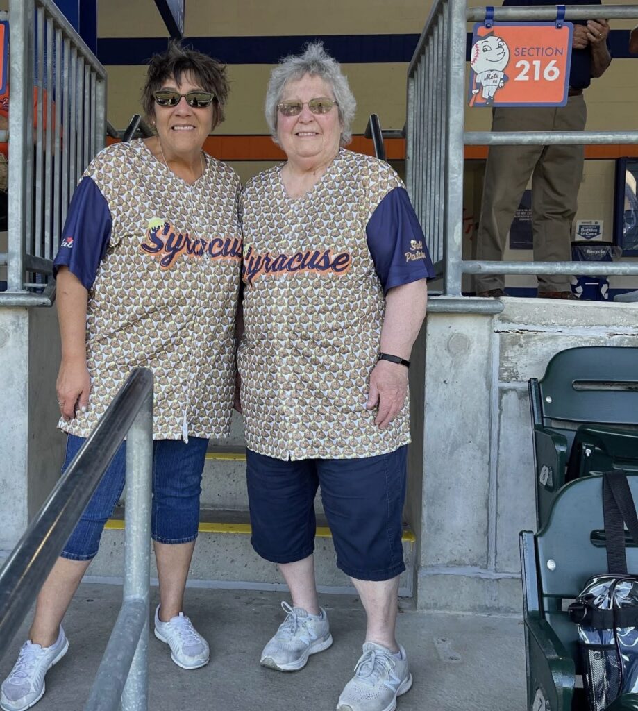A woman and her mother stand together for a picture at a baseball game.