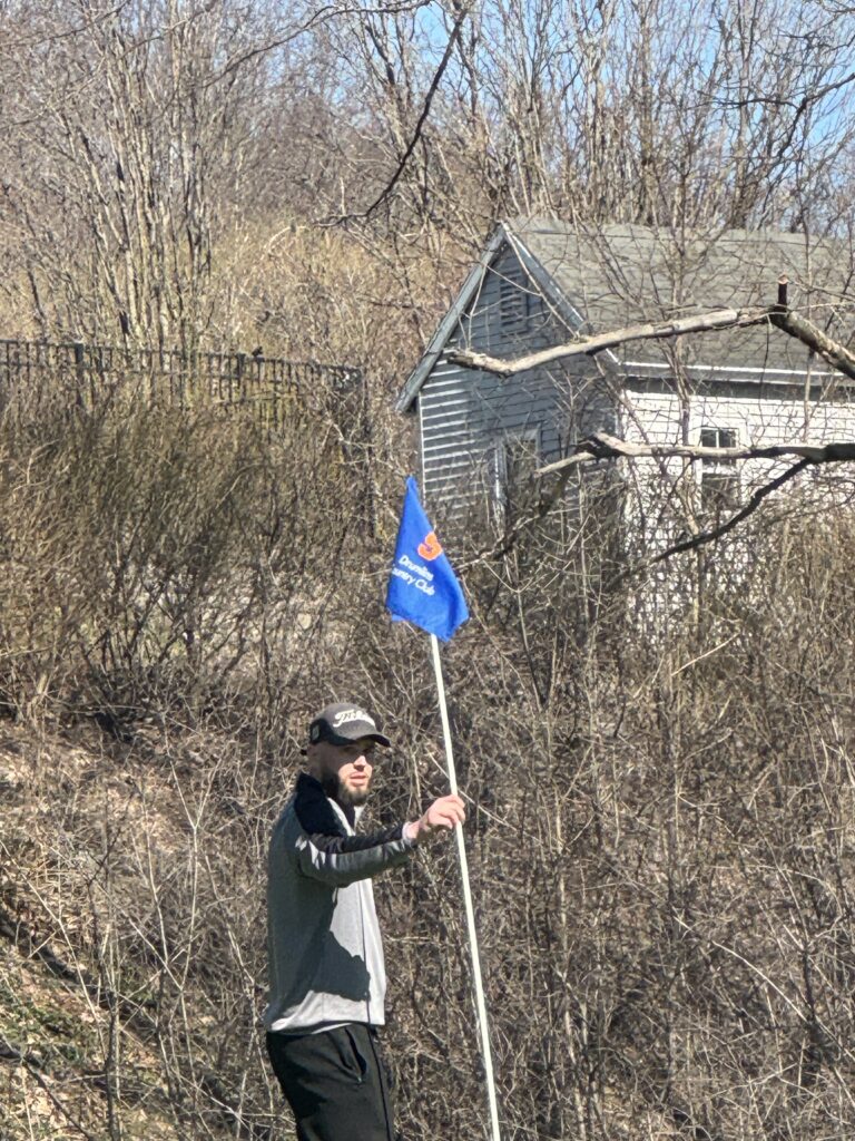 A golfer holding the flag pole with a Drumlins Country Club Flag waving