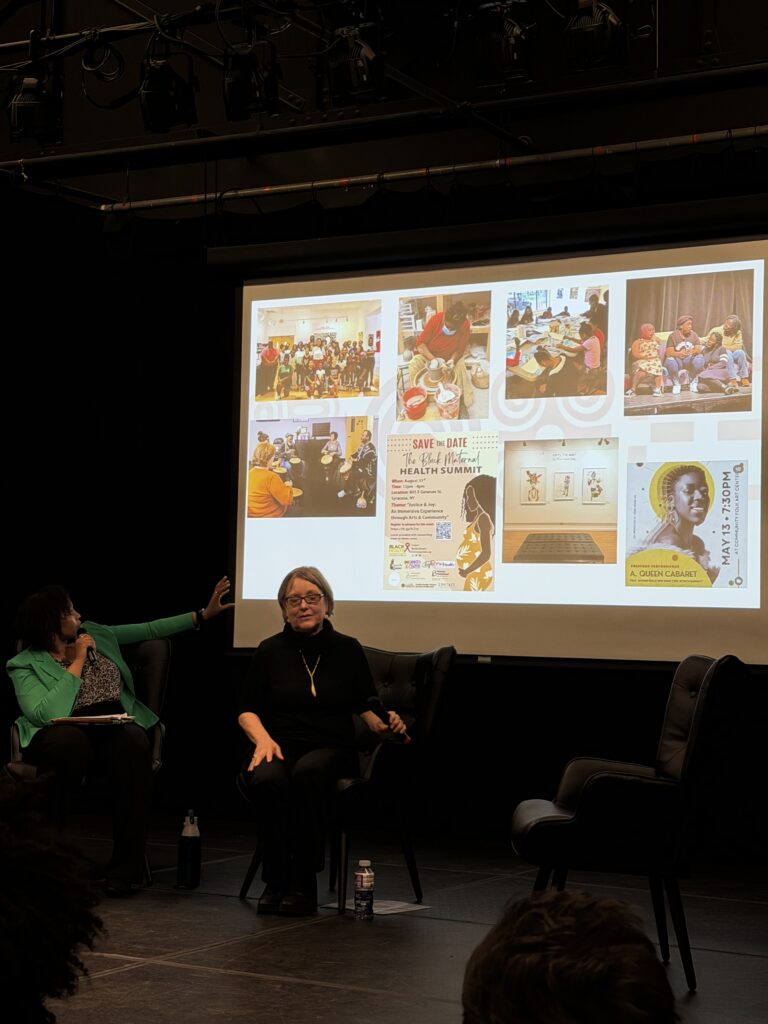 Two women in front of a presentation screen, with one of them pointing towards the screen.