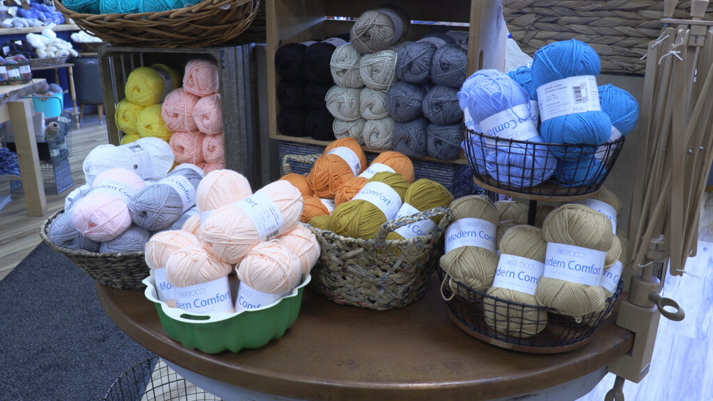Baskets and shelves filled with colorful balls of yarn in pink, orange, blue, yellow and tan at a local yarn store.