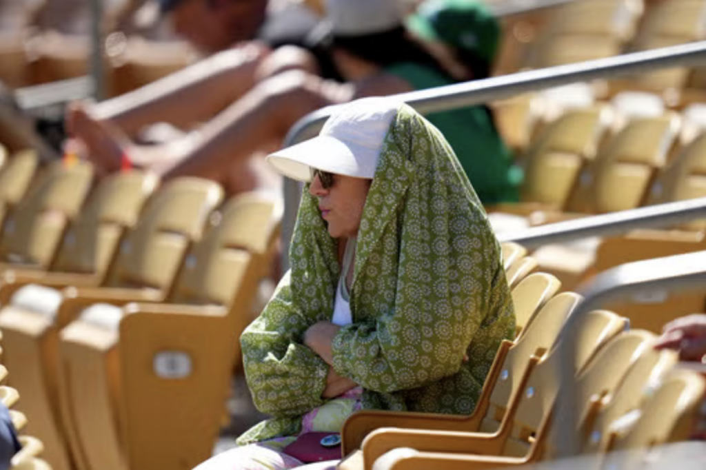 A woman in stadium seating wearing a cloth over her head and shoulders to block the sun.