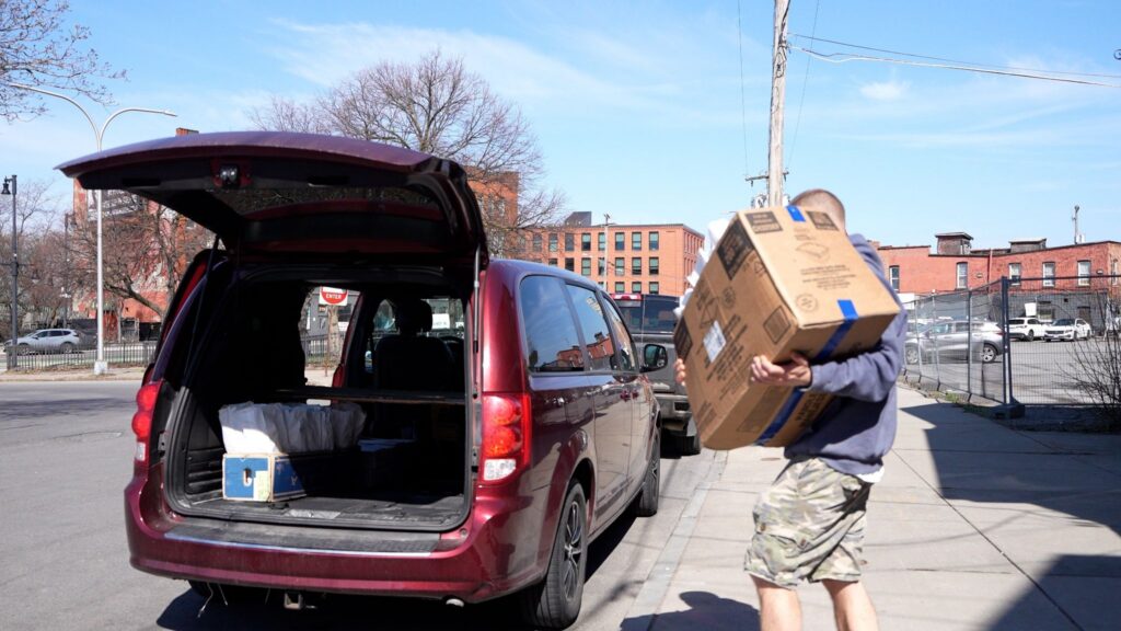 Man bringing box of bread out to a red van with the trunk open