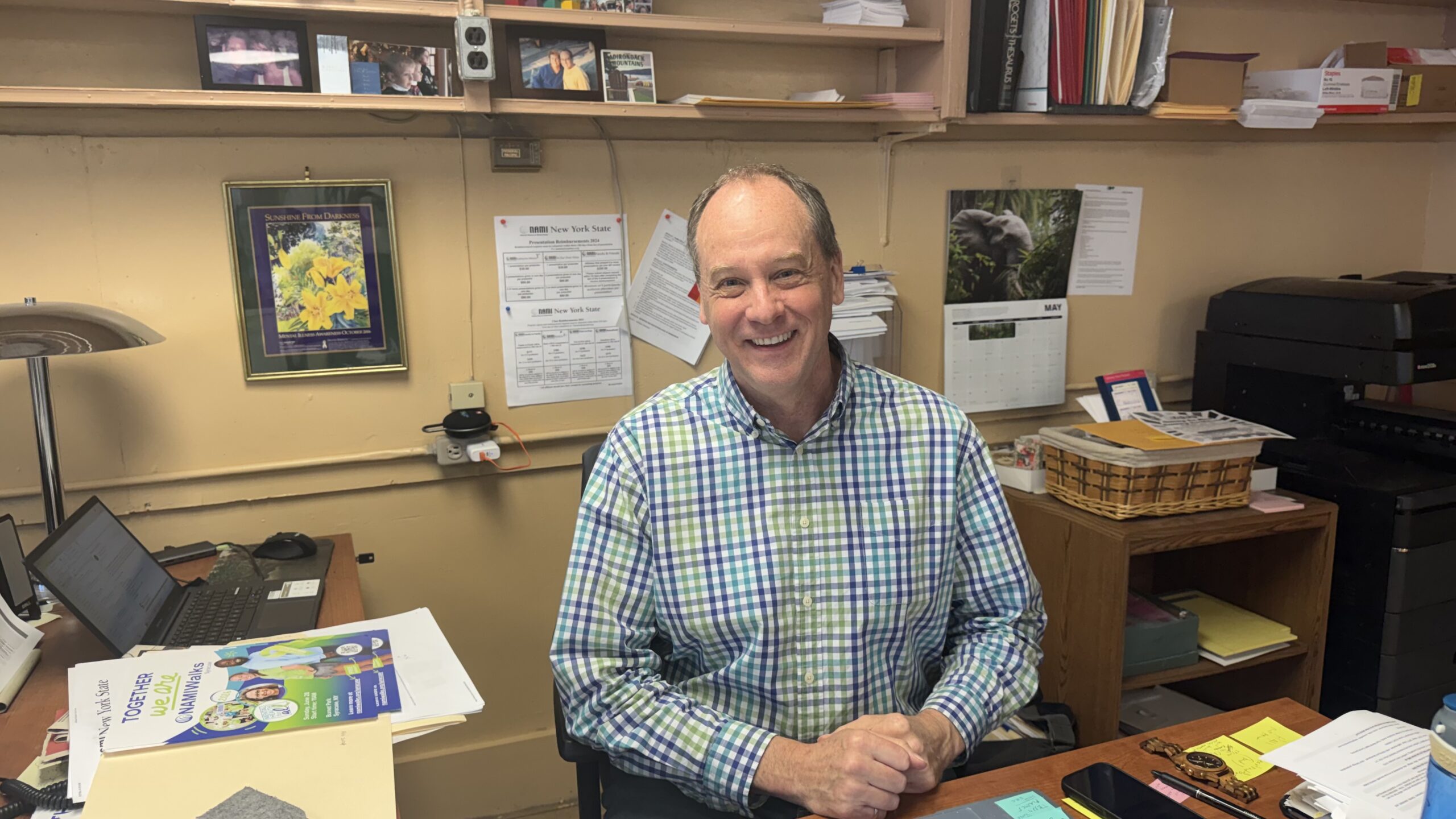 Man smiling, sitting at desk at National Alliance on Mental Illness Syracuse