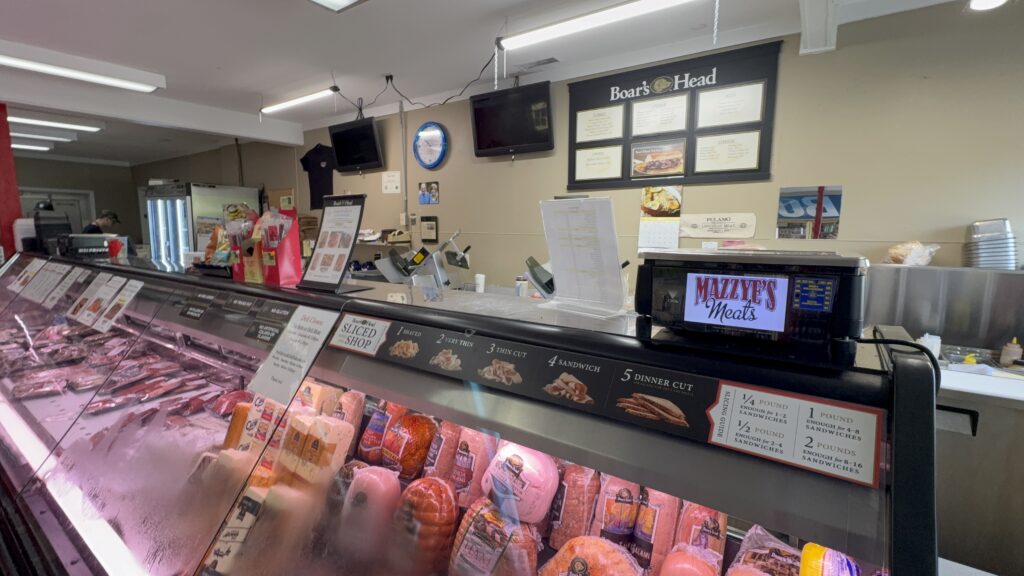 A deli counter filled with sliced meats and cheeses at Mazzye’s Meats, with signage showing cut thickness options and portion guidelines.