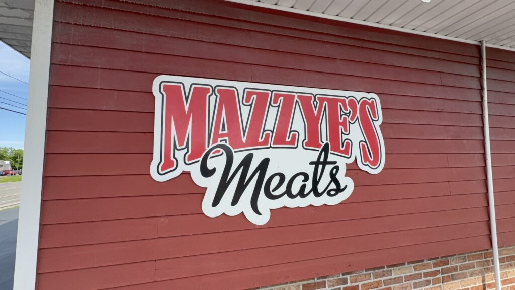 The exterior sign of Mazzye’s Meats on a red wooden building, with bold lettering identifying the butcher shop.