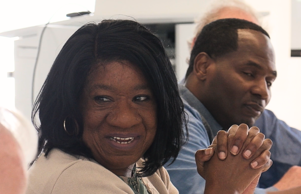 A women smiling with her hands crossed sitting next to a man.