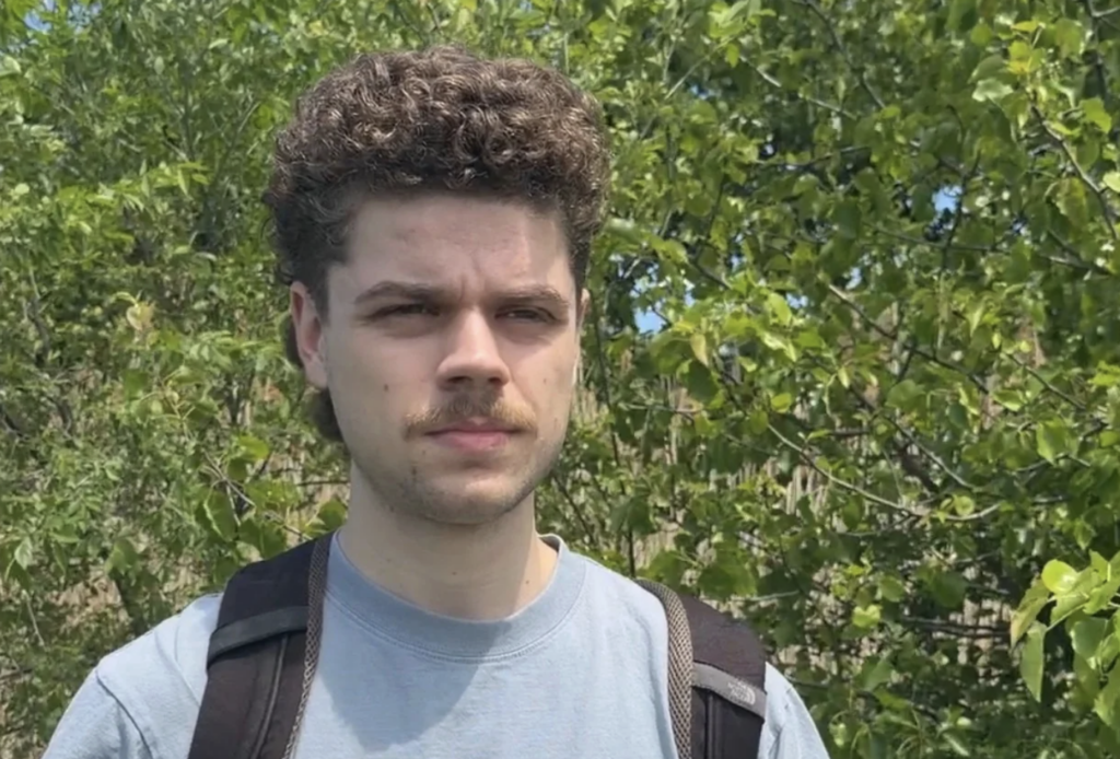 Young man with curly hair and a mustache from shoulder up