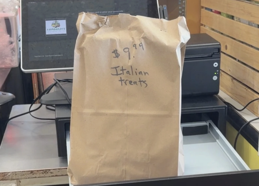 Brown paper bag near a cash register that has "$9.99 Italian Treats" written in sharpie