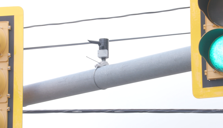 Gray pole with a small camera beteen two traffic lights.