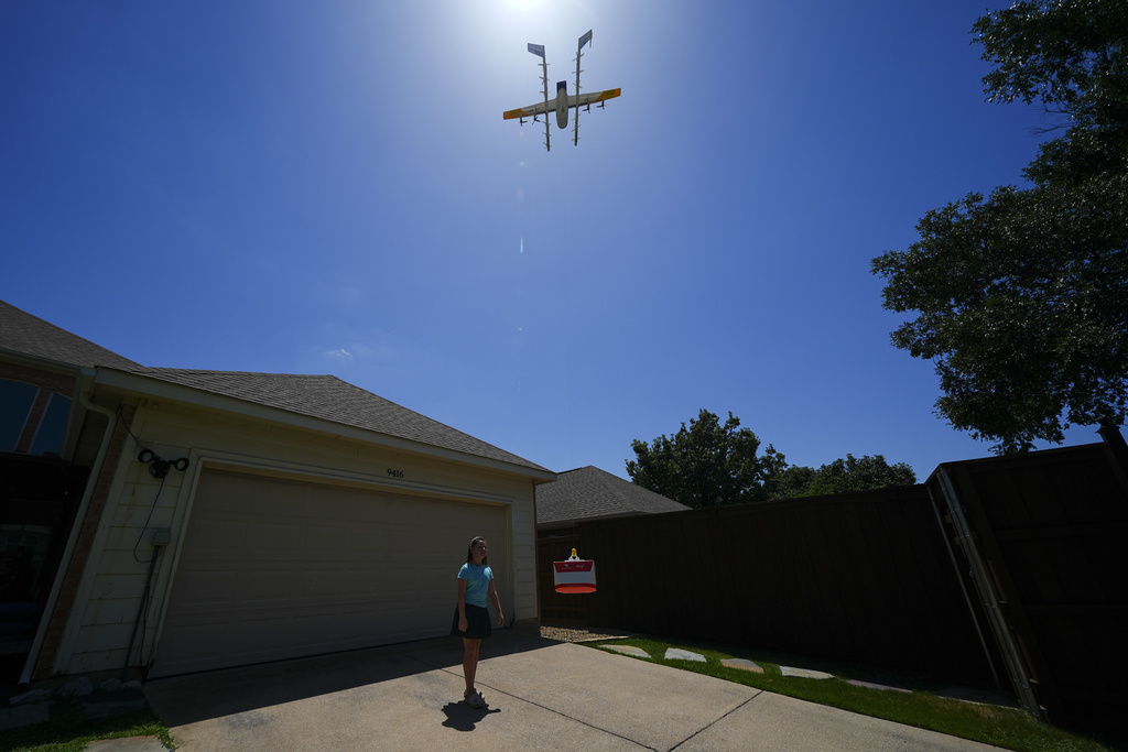 A little girl in her driveway set to gather a package delivered from a drone. 