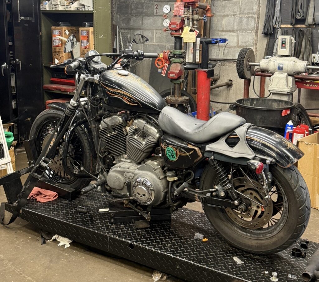 A black Harley-Davidson motorcycle on a service lift inside a motorcycle repair shop.