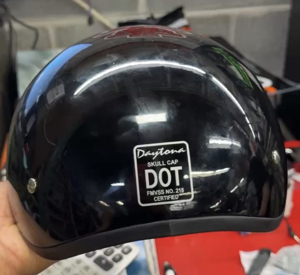 A black motorcycle helmet with a DOT certification sticker displayed on the back.