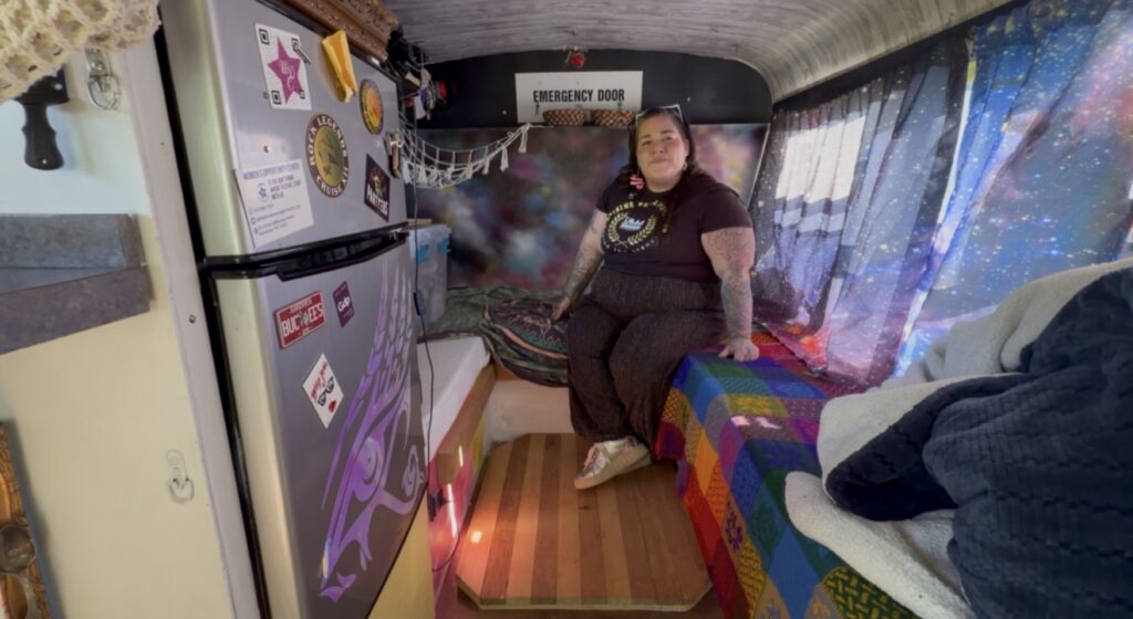 Aldea Girard sits inside her converted mini bus RV surrounded by colorful galaxy-themed décor, a small kitchen area and living space she helped build during a two-year renovation project.