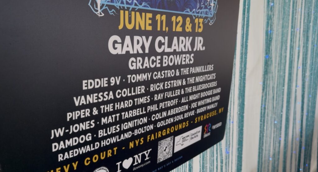 A poster displays the lineup for the 2026 New York State Blues Festival, including headliner Gary Clark Jr. and other featured performers.