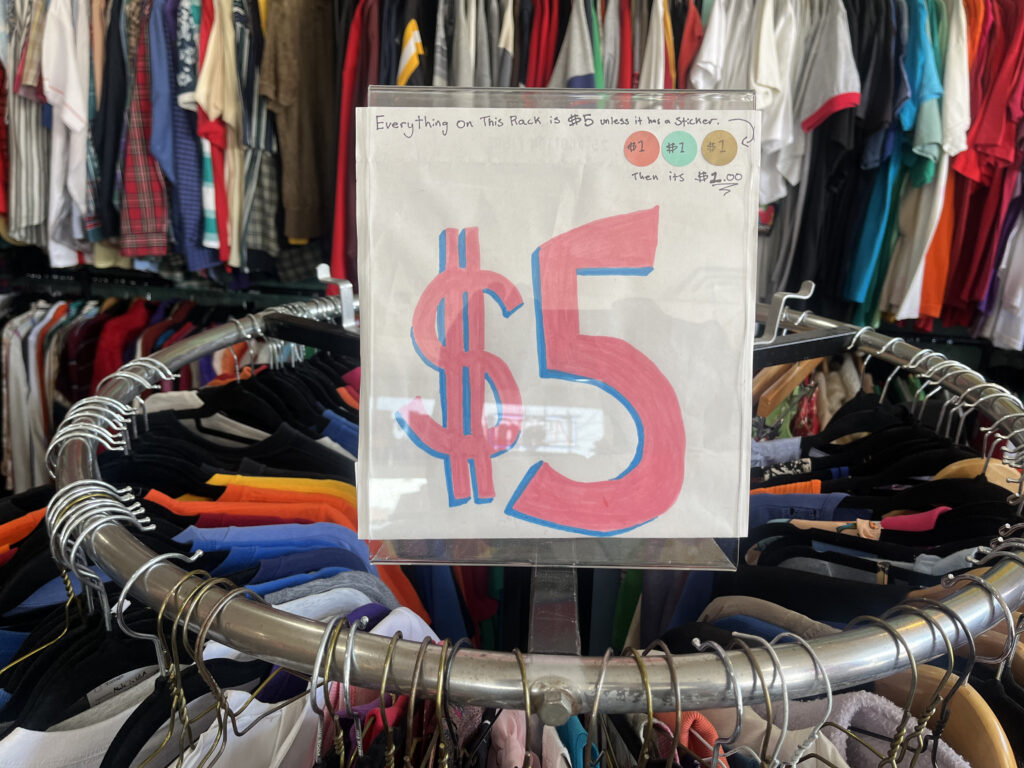 A five-dollar signs sits atop a clothing rack. 