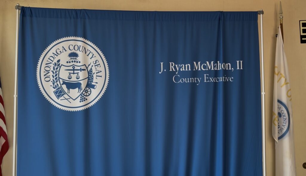 Blue Sheet with Onondaga county logo and Ryan McMahon's name hangs up in room.