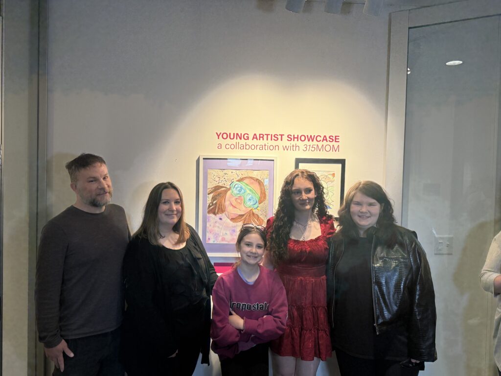 Madilynne Madore stands with family members in front of her artwork at the Young Artists Showcase exhibition inside the Everson Museum of Art.