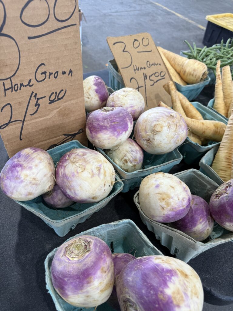 Purple-top turnips and parsnips displayed in green cartons for sale at the CNY Regional Market.