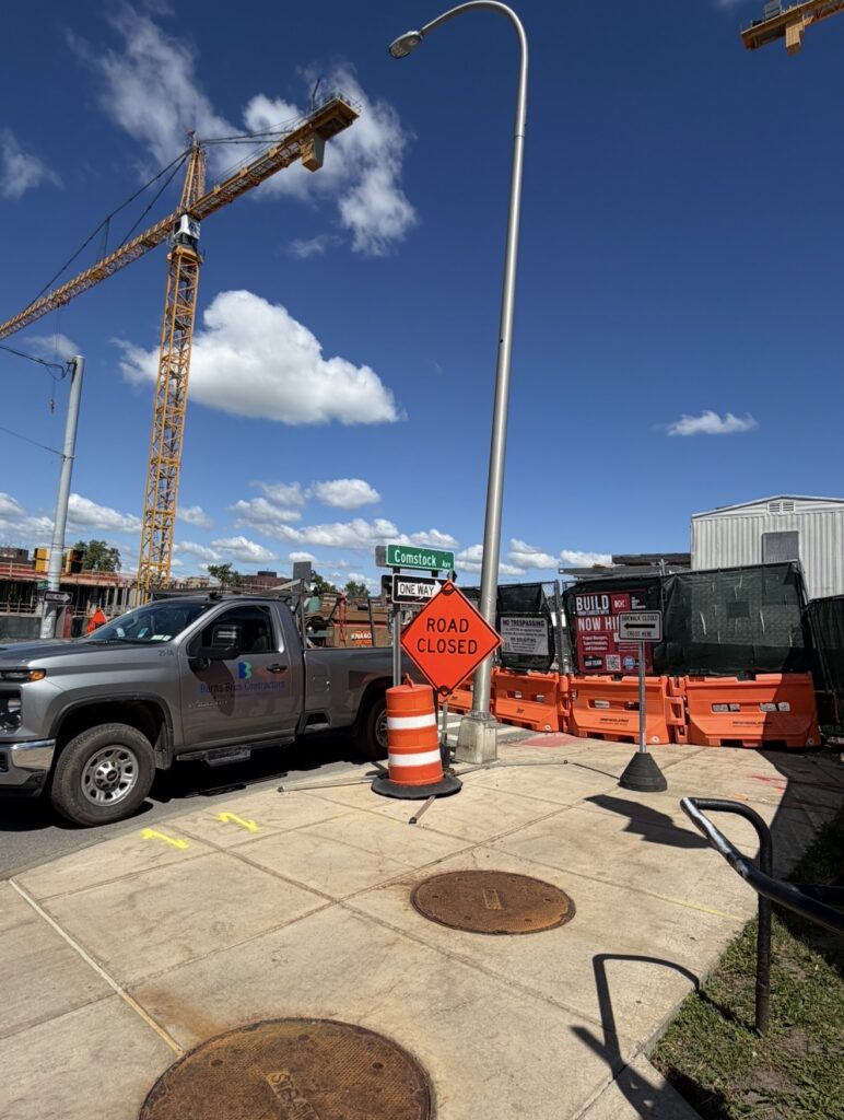 Road closed sign and Comstock Ave street sign in front of a grey truck and constructiuon site 