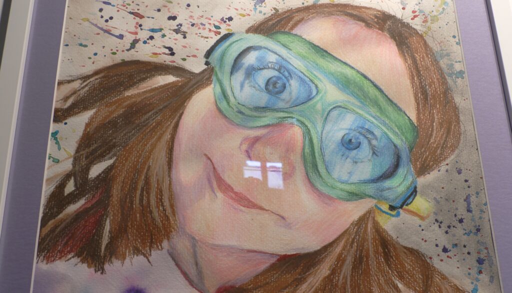 Close-up view of Madilynne Madore's mixed-media portrait featuring her younger sister wearing swim goggles.