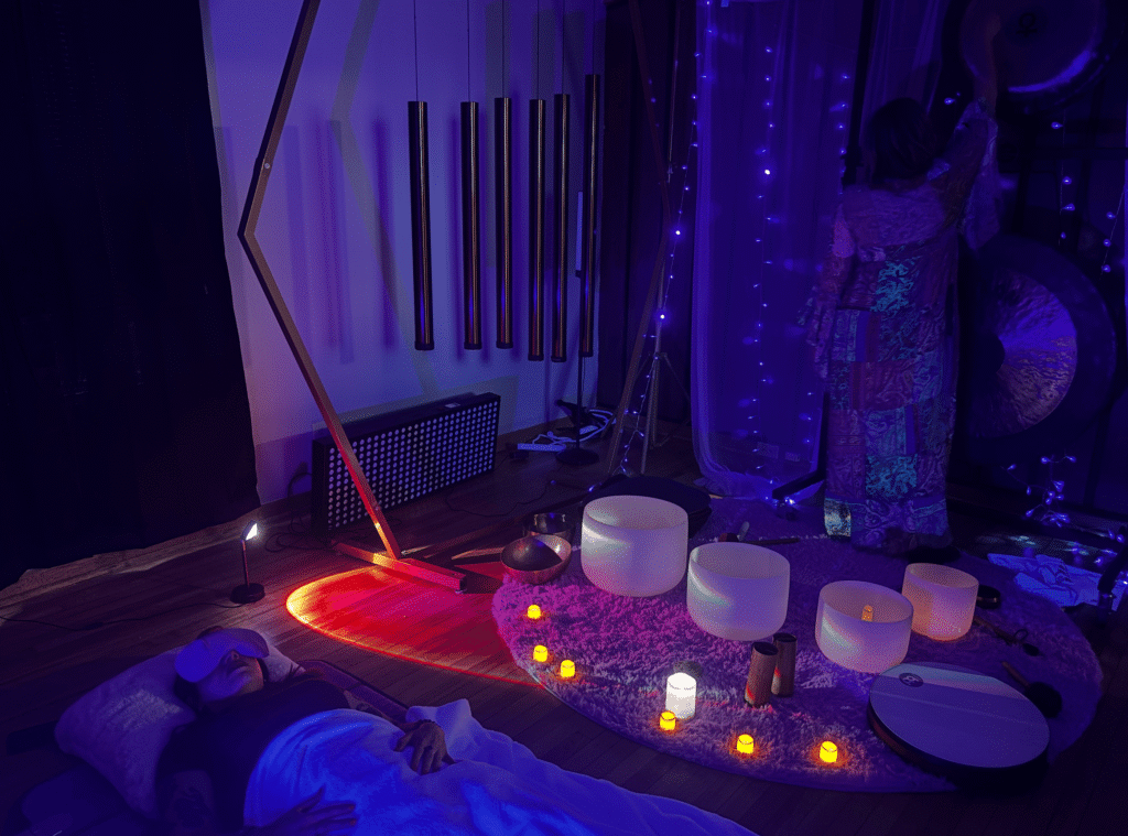 A sound bath practitioner plays a gong while one of her class participants is lying on the ground.