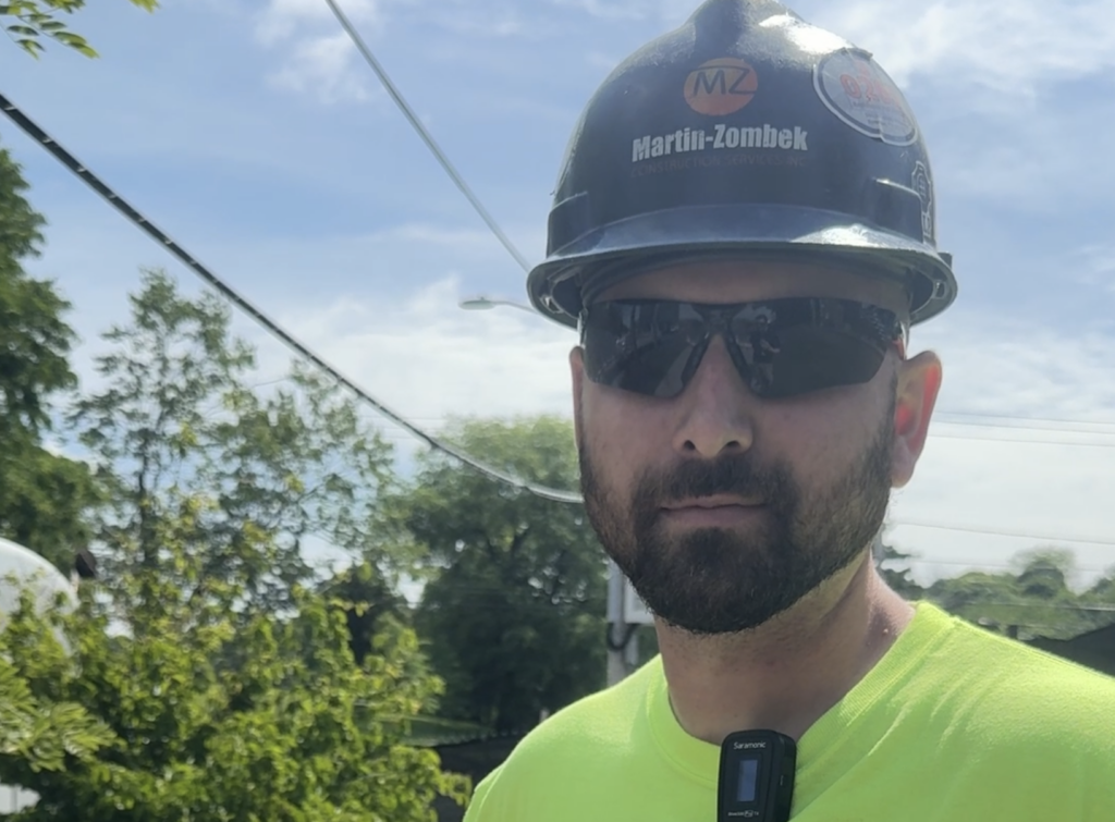 Bearded man in blue hard hat, sunglasses and neon green shirt.