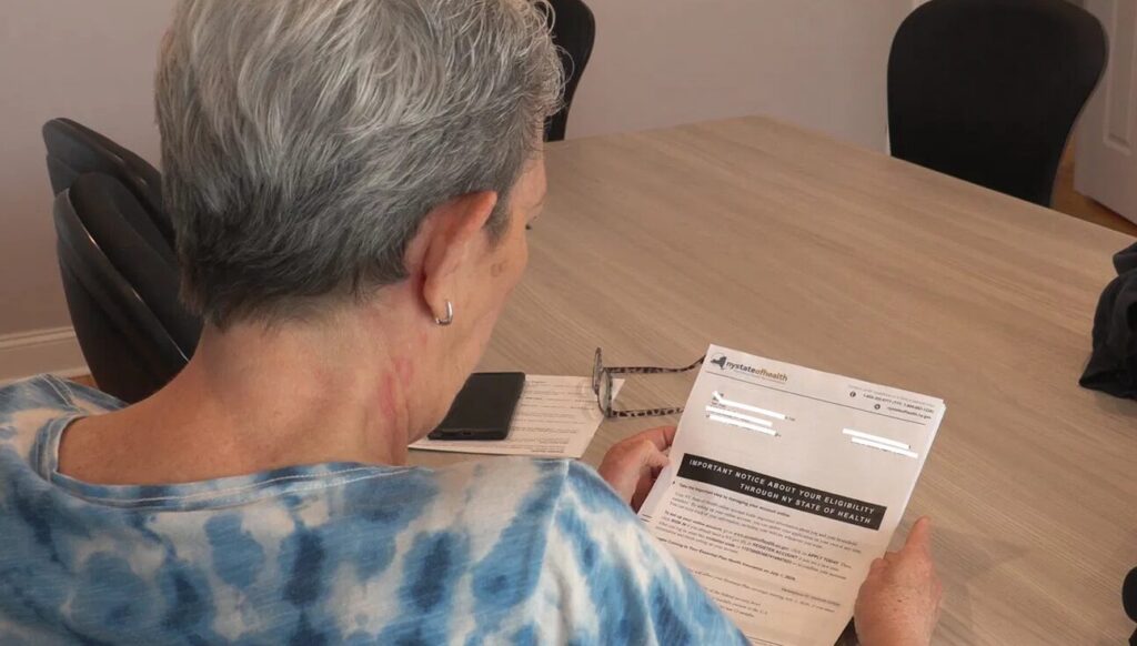 A woman sits at a table reading a letter from NY State of Health marked "Important Notice About Your Eligibility."