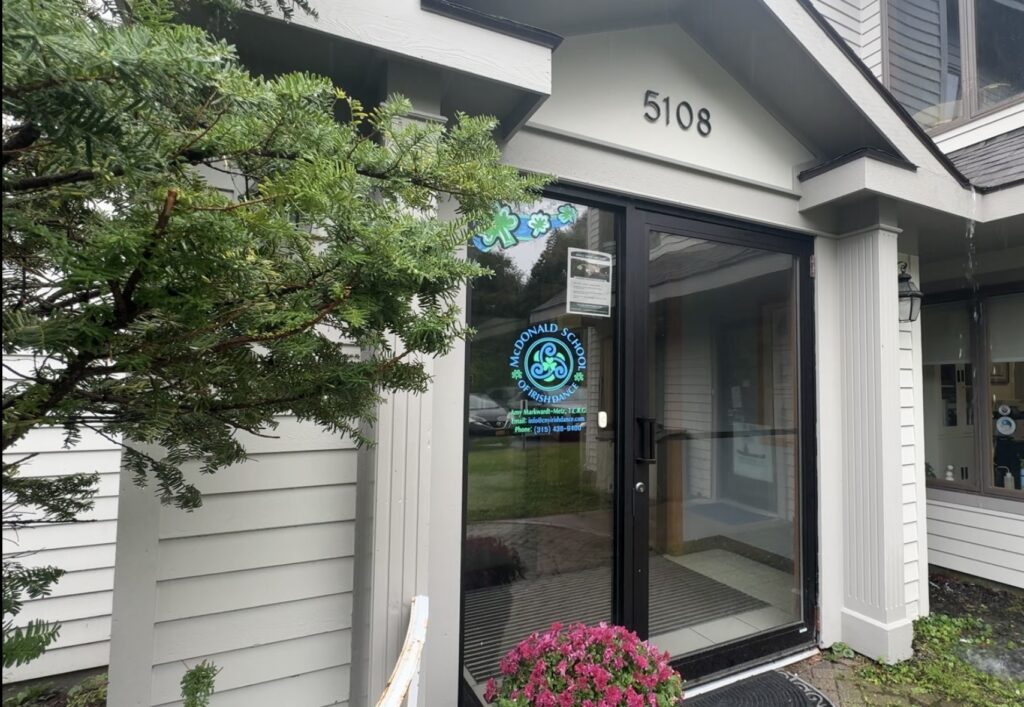 Glass entrance door to the McDonald School of Irish Dance, displaying the school's logo, photographed on a rainy day.