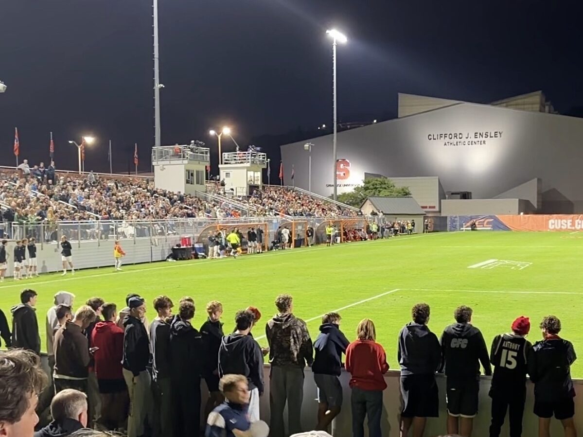 Picture of fans standing on boards and field and stadium filled with people in the background
