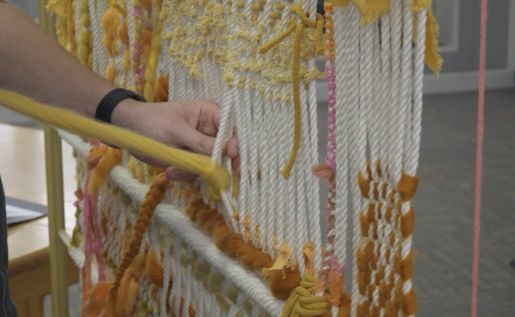 Hands weaving through Monet's macramé canvas