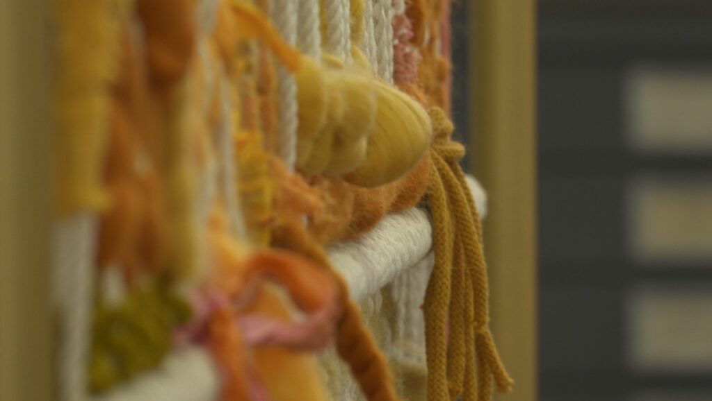 Threads of yarn hanging from a macramé portrait