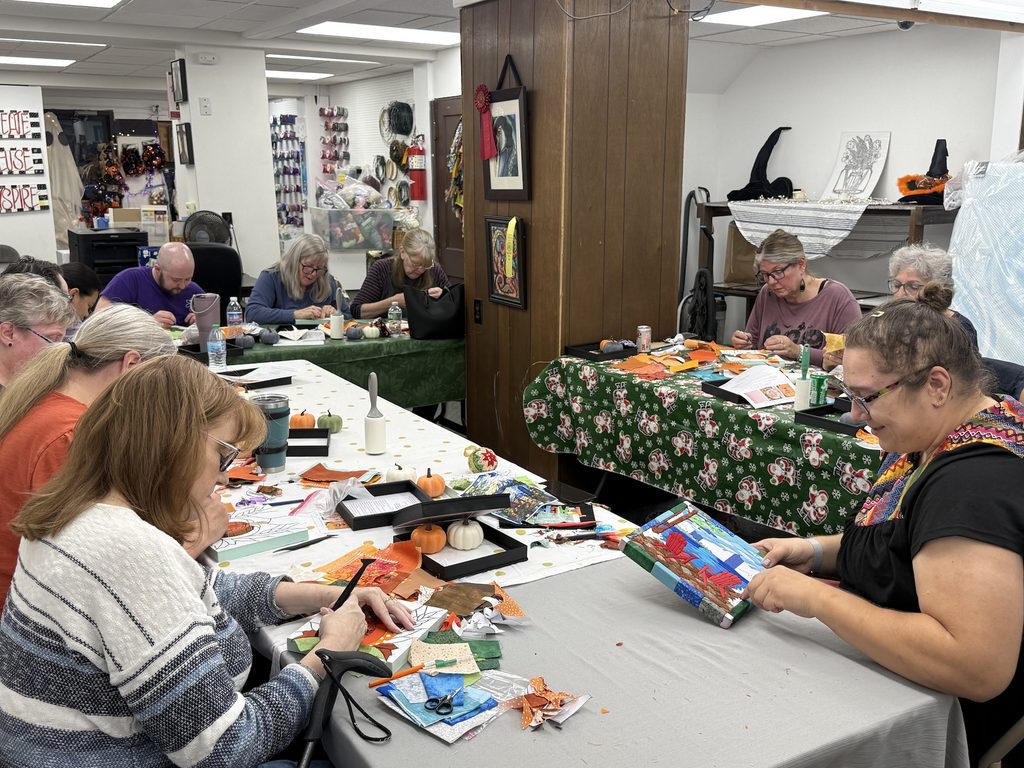 People participate in a craft session, creating artwork with colorful fabric, paper and other art supplies at tables.