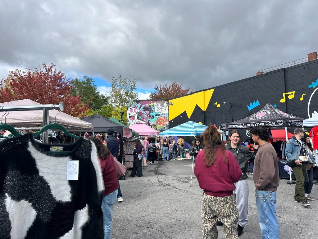 Shoppers mingle among tents at The Sound Garden, with knit sweater from Small Rack in the foreground and murals behind.
